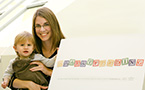Sarah Thompson holds her son Ryan beside a sign promoting the breastfeeding campaign.